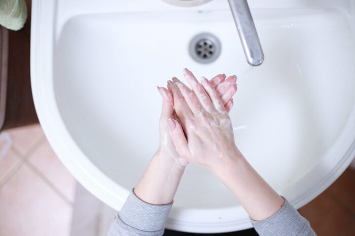 someone washing their hands in a white sink after feeding raw dog food, the myth that raw dog food is not safe can be avoided if owners practice safe hygiene practices, as they would when handling their own raw meat